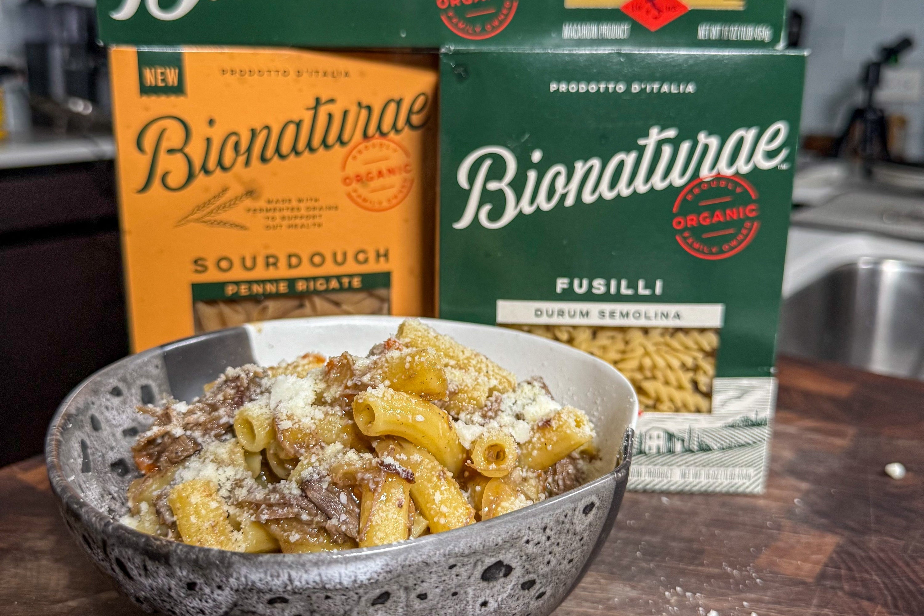 Bowl of Pasta Alla Genovese topped with grated cheese in a ceramic bowl with Bionaturae pasta boxes in the background
