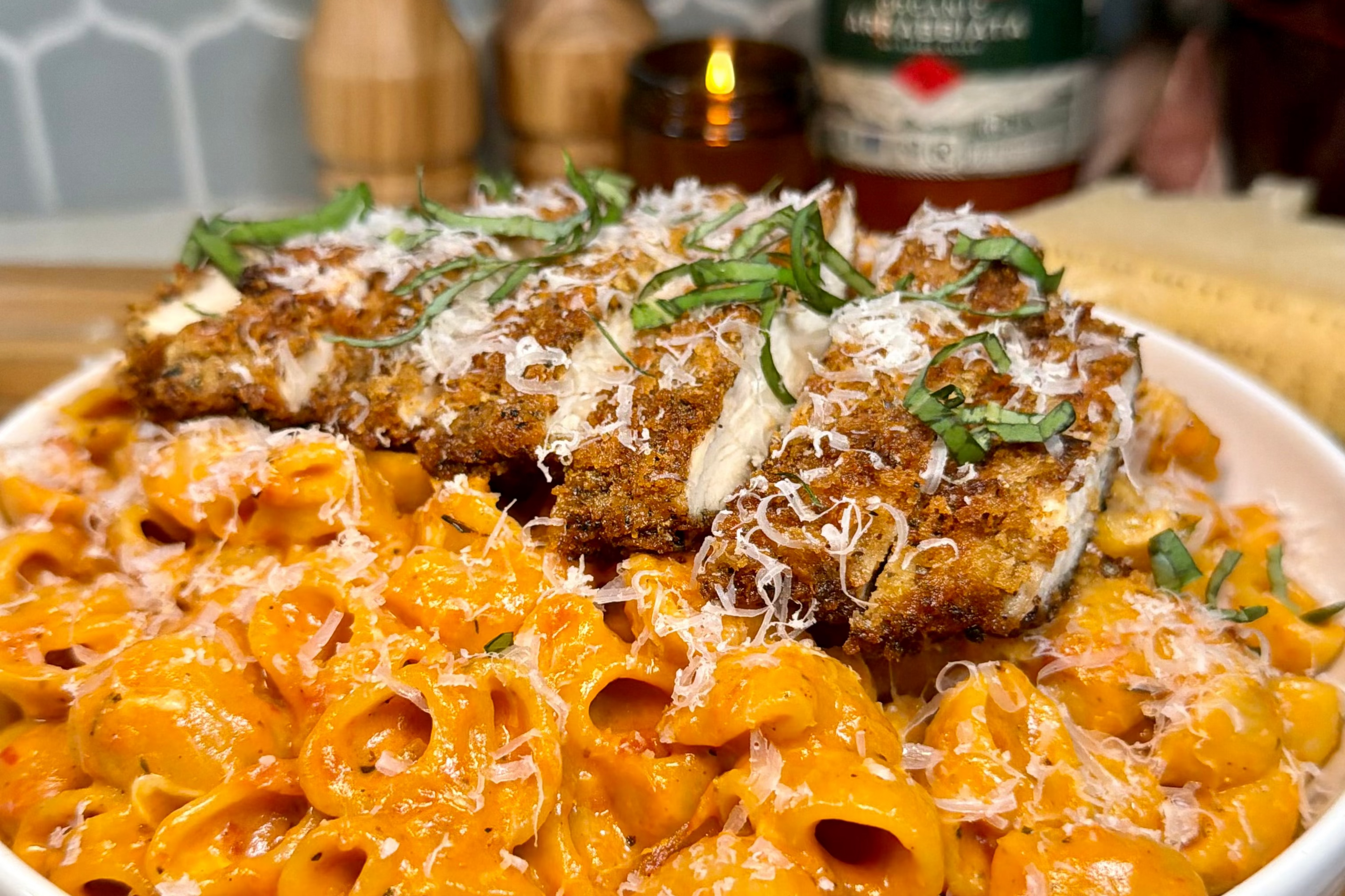 Breaded chicken cutlets served over creamy tomato pasta in a white bowl, topped with grated Parmesan and sliced basil