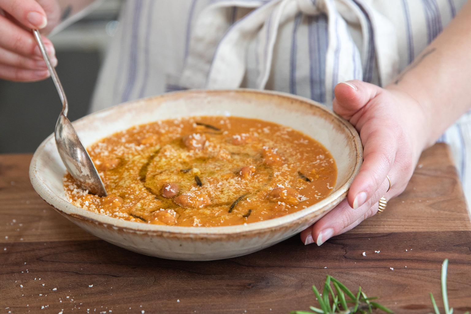 Person holding a bowl of creamy borlotti bean soup with a spoon over a wooden table