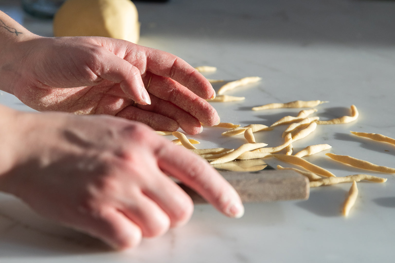 Hands shaping egg-free Einkorn pasta strands on a marble countertop in natural light