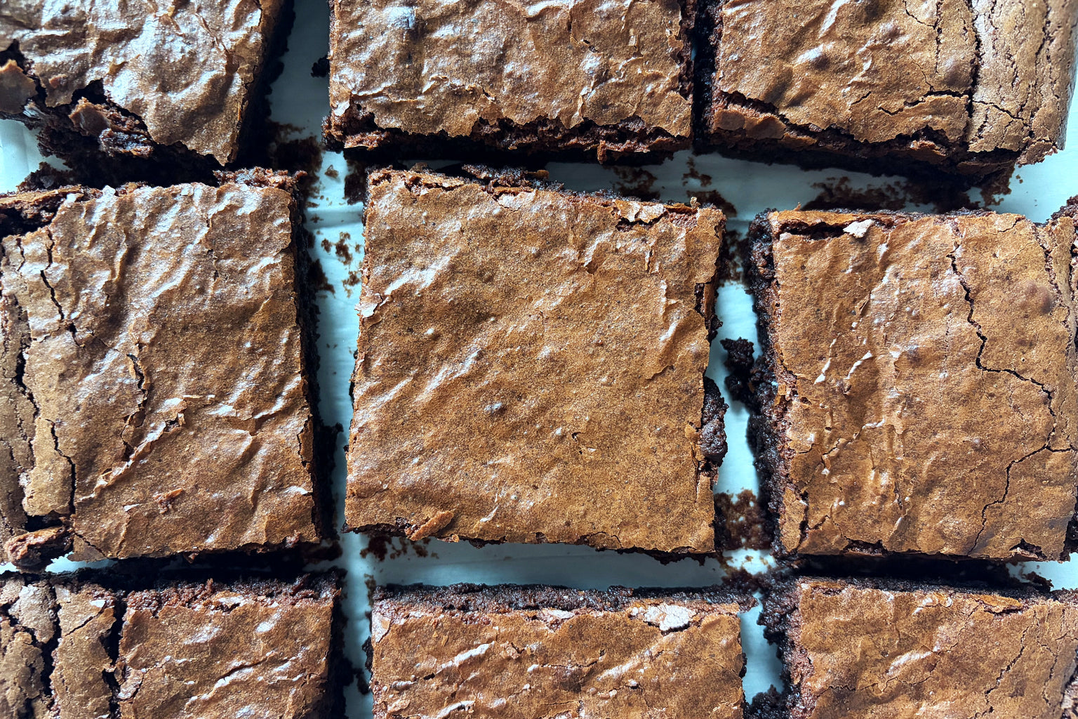 Top view of sourdough einkorn brownies cut into squares showing crackly glossy crust and fudgy interior on a white baking tray