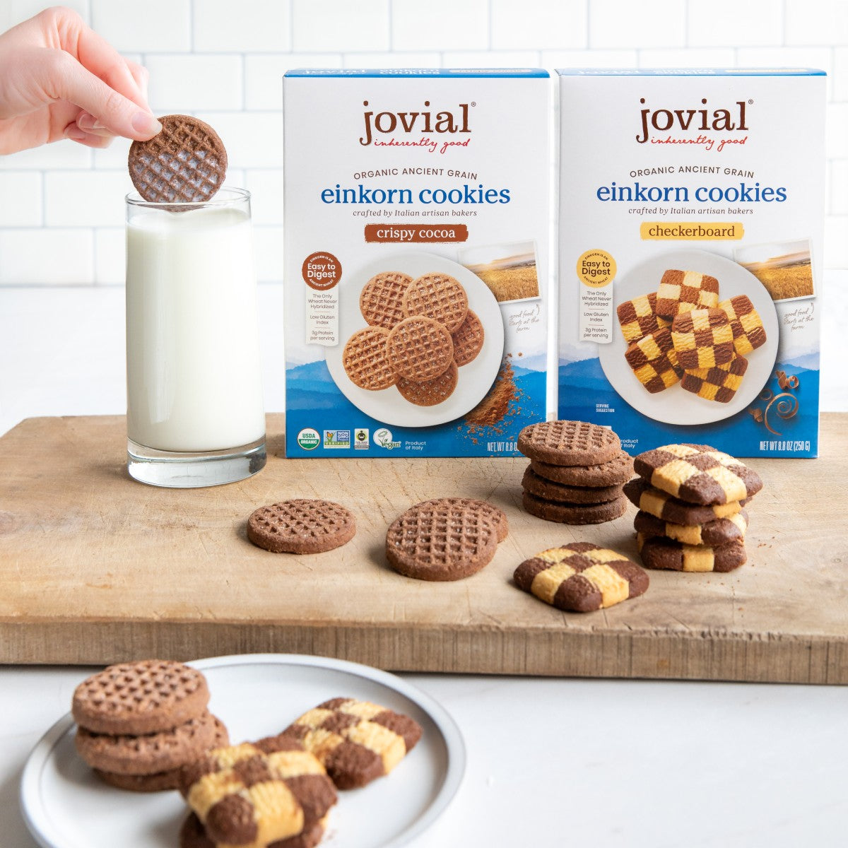 Front view of Jovial organic Einkorn cookie boxes and cookies showing crispy cocoa and checkerboard cookies with glass of milk