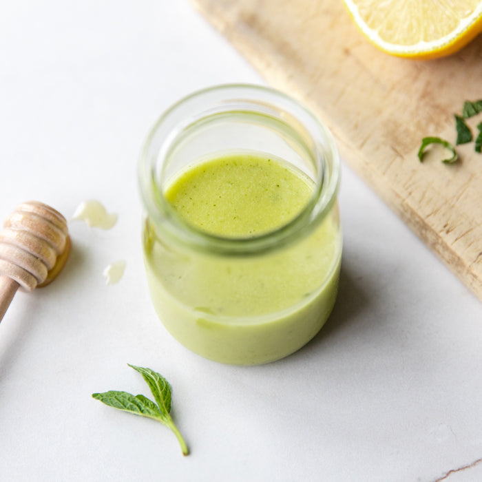 Top-down jar of mint, honey and lemon dressing showing creamy pale-green texture with honey dipper and mint
