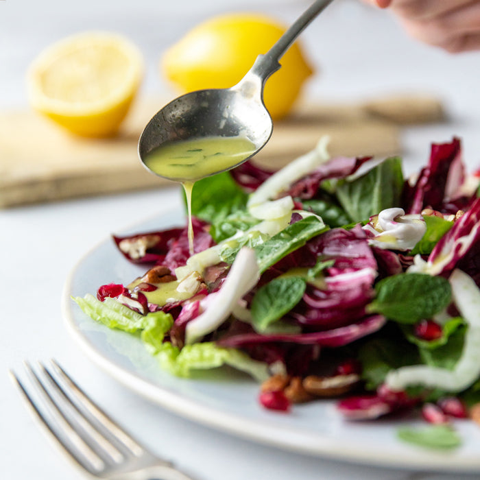 Spoon drizzling mint, honey and lemon salad dressing over mixed radicchio and lettuce with lemon halves in background