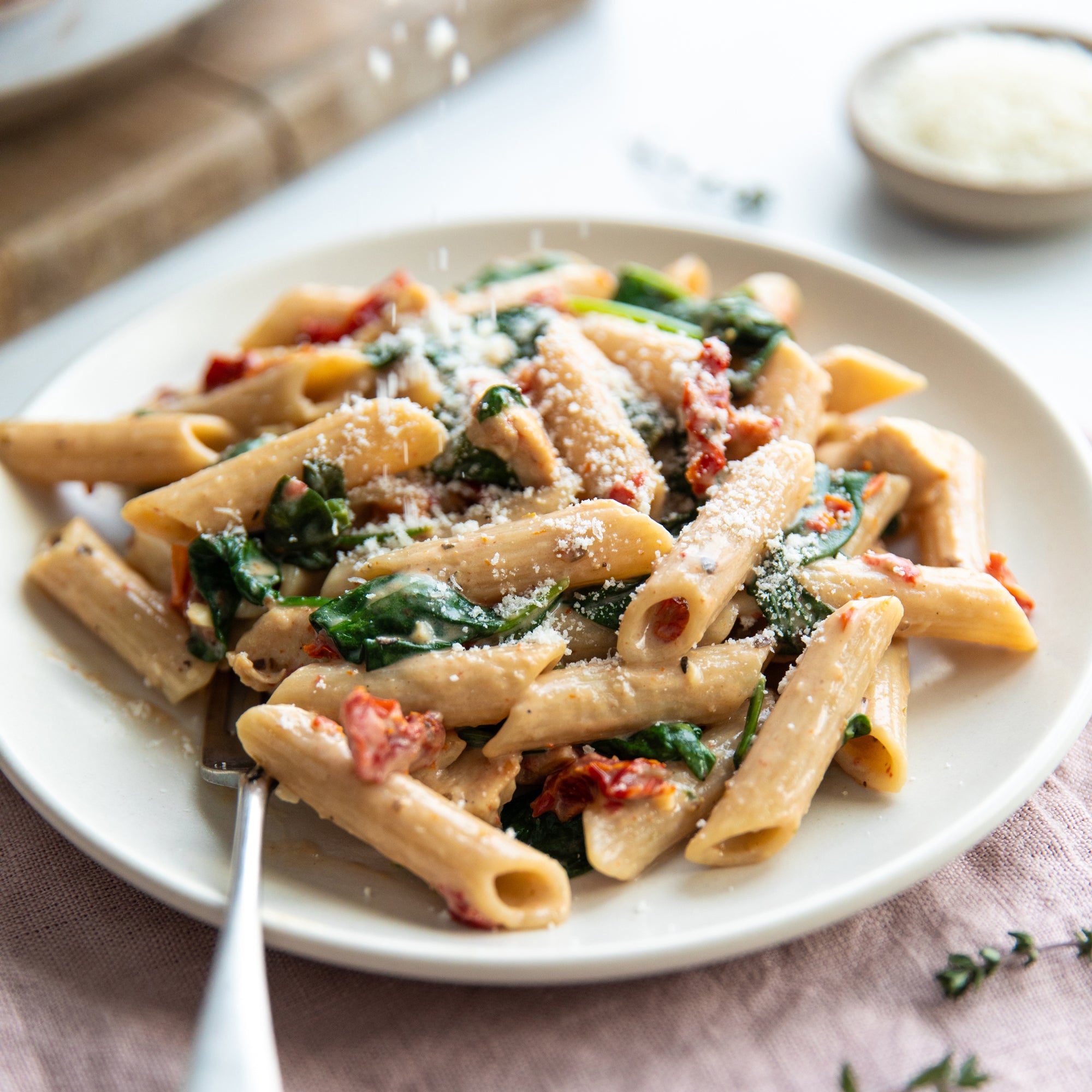 Marry Me chicken pasta with gluten-free penne, spinach, sun-dried tomatoes and grated cheese on a white plate with a fork