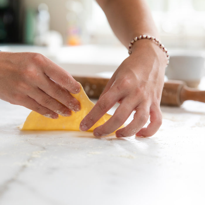 Hands folding einkorn chapatti dough on a floured countertop with a wooden rolling pin in the background