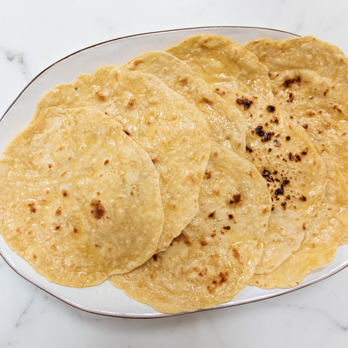Top-down view of Einkorn chapatti flatbreads showing golden, lightly charred surface and oil sheen on a white oval plate
