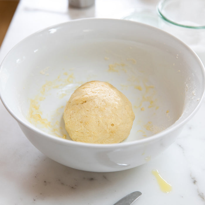 Ball of einkorn chapatti dough resting in a white mixing bowl on a marble countertop