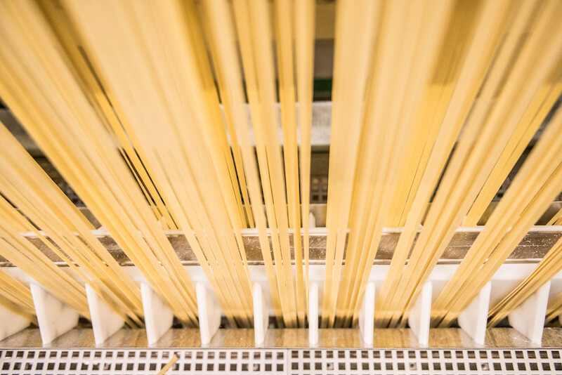 Top-down view of long spaghetti-style pasta strands on drying racks showcasing uniform extrusion in an artisan pasta factory