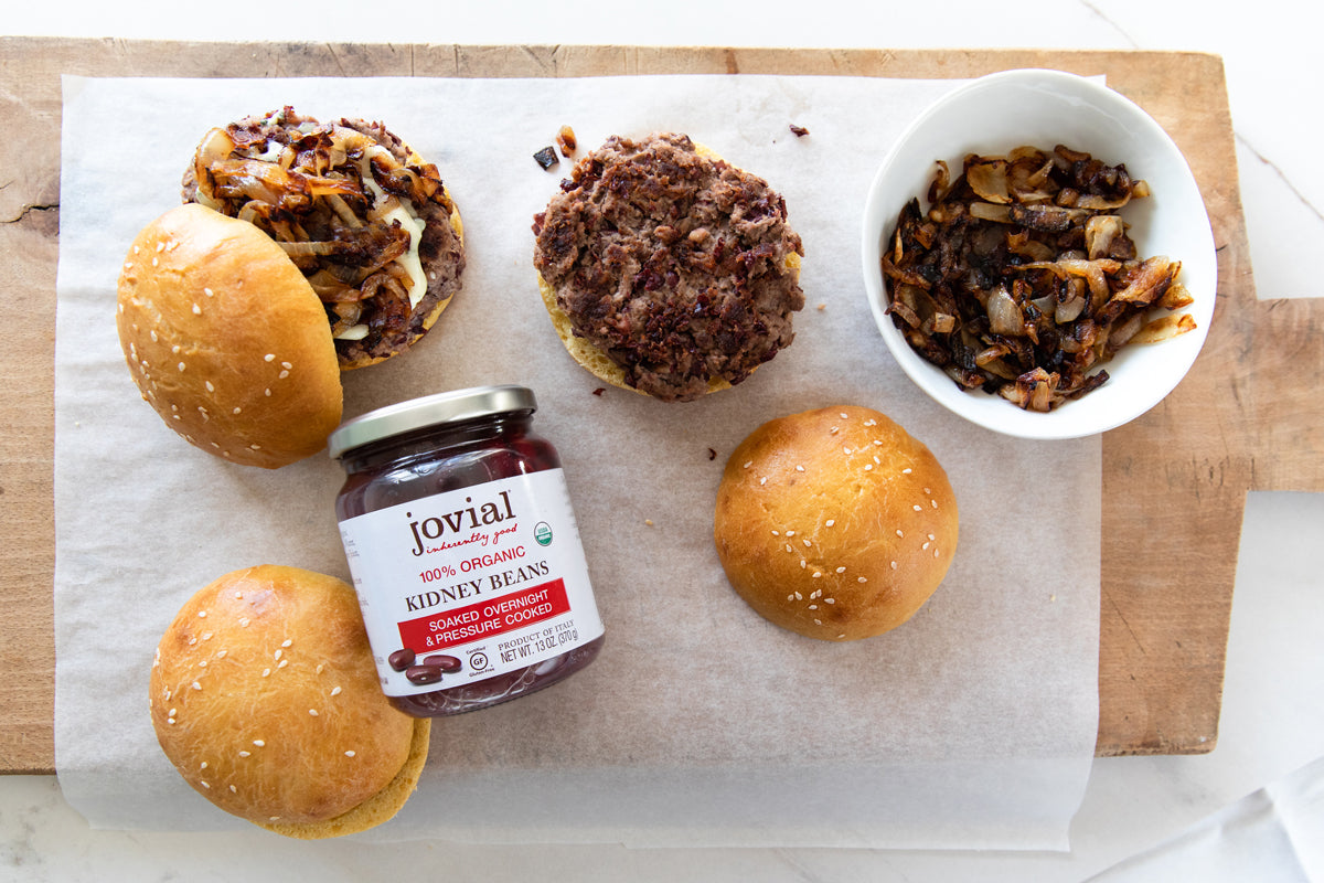 Kidney bean burger patties and buns with a jar of Jovial organic kidney beans and caramelized onions on a wooden board