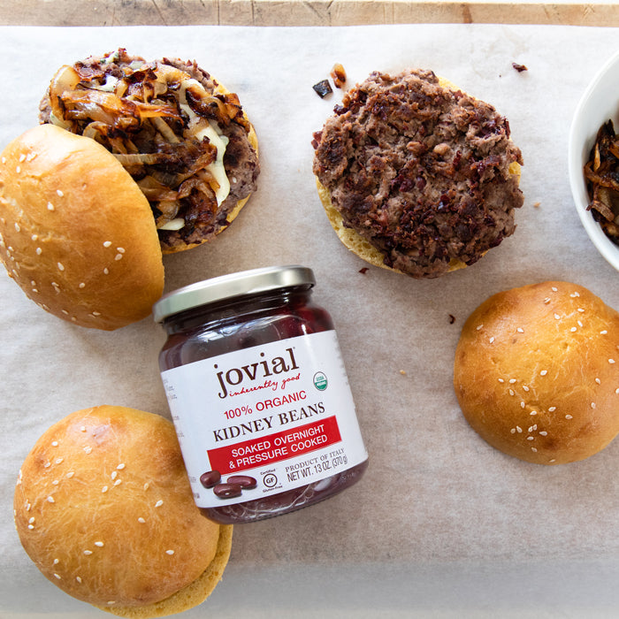 Top-down view of a jar of Jovial 100% Organic Kidney Beans with two homemade kidney bean burger patties and sesame buns on parchment