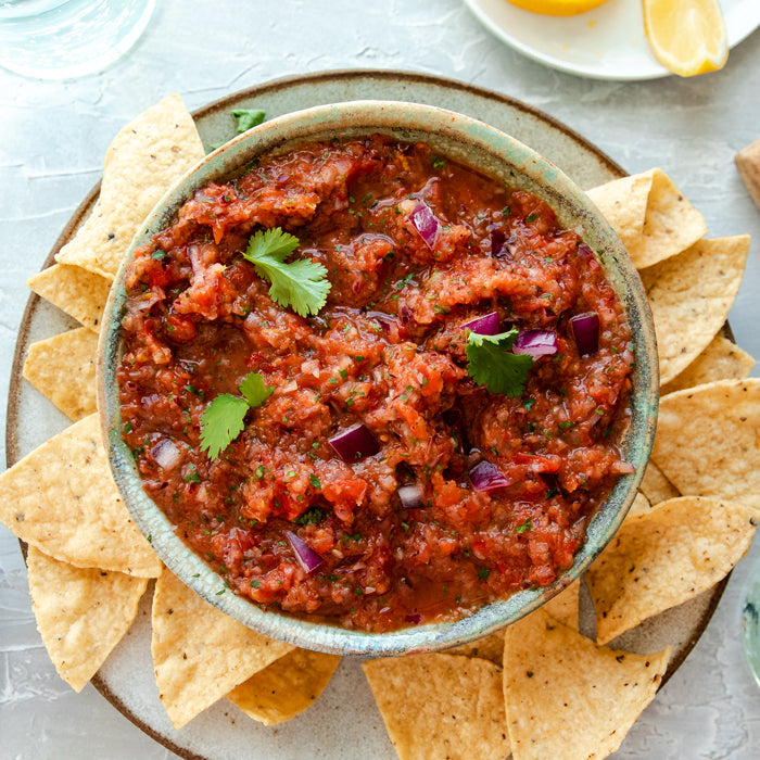 Top-down view of roasted red pepper and tomato salsa with cilantro and diced red onion, served with tortilla chips