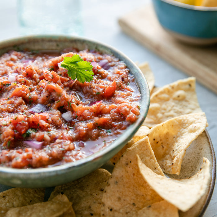 Close-up of roasted red pepper and tomato salsa with chunky texture and cilantro garnish next to tortilla chips