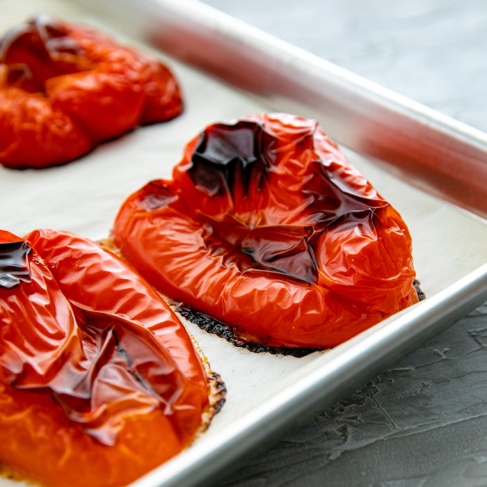 Roasted red pepper halves blistered and charred on a parchment-lined baking sheet