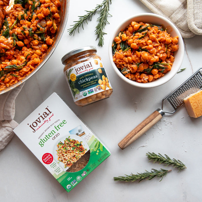 Top-down view of Jovial gluten-free orzo box and jar of organic chickpeas with a bowl of saucy tomato chickpeas and orzo