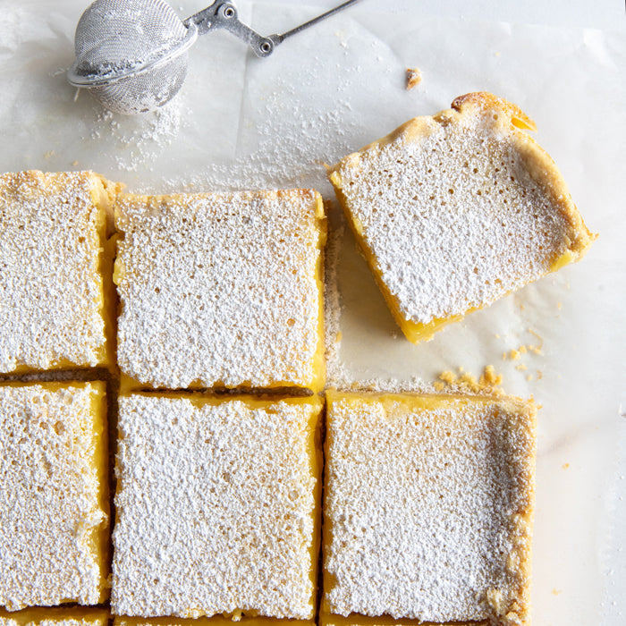 Top-down view of Einkorn lemon bars cut into squares and dusted with powdered sugar on parchment paper