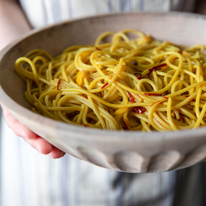 Saffron spaghetti in a ceramic bowl held by a person, glossy noodles with saffron threads and red pepper flakes