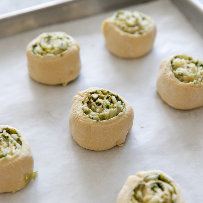 Close up of unbaked Einkorn pizza dough spirals filled with cheesy leek and pesto on a parchment-lined baking sheet