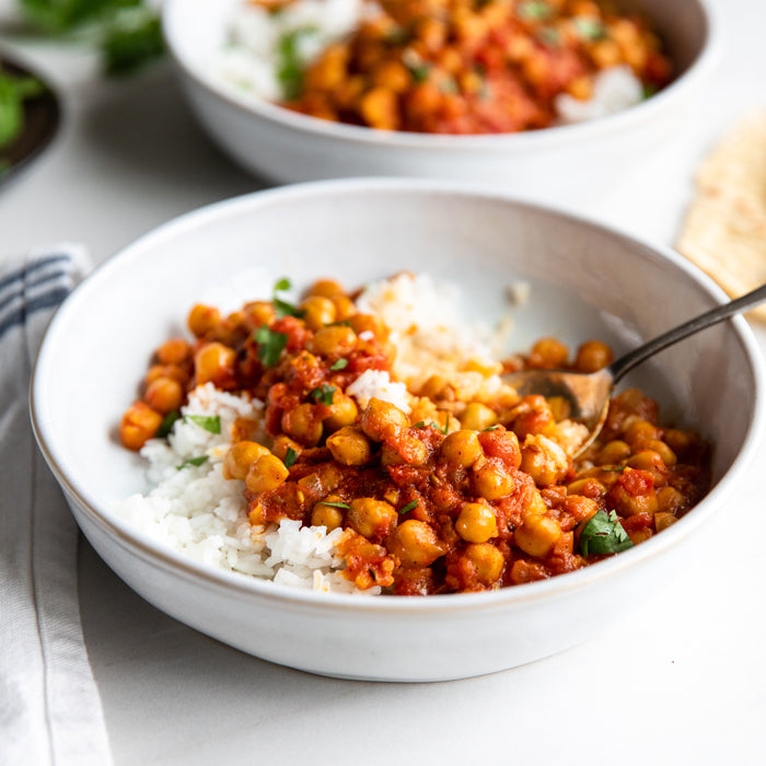 Vegan chickpea curry spooned over white rice in a shallow bowl with cilantro garnish and a spoon