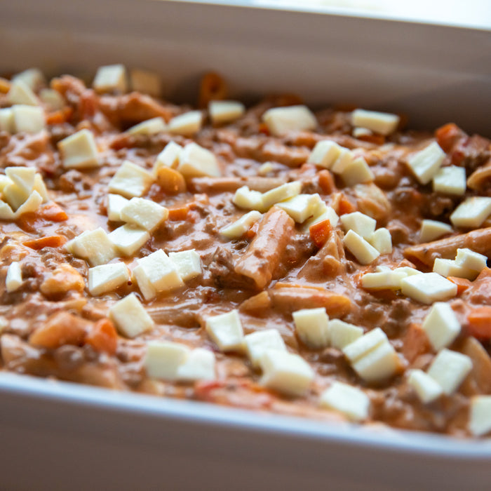 Close-up of sourdough penne al forno in a baking dish with tomato-béchamel sauce, ground meat, and mozzarella cubes