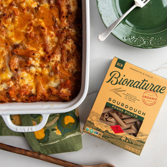 Baked sourdough penne al forno in a white baking dish beside an organic Bionaturae Sourdough Penne box on a marble surface