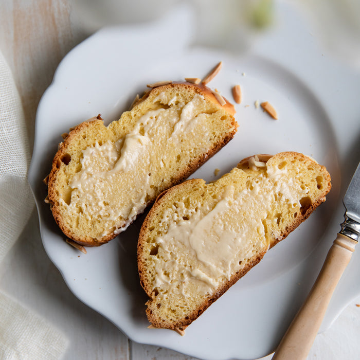 Top-down view of two slices of Einkorn Easter bread spread with butter, almond slivers on a white scalloped plate with a butter knife