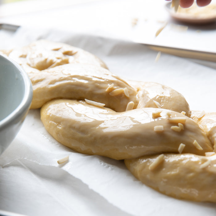 Braided einkorn Easter bread dough being brushed with egg wash and sprinkled with slivered almonds on parchment