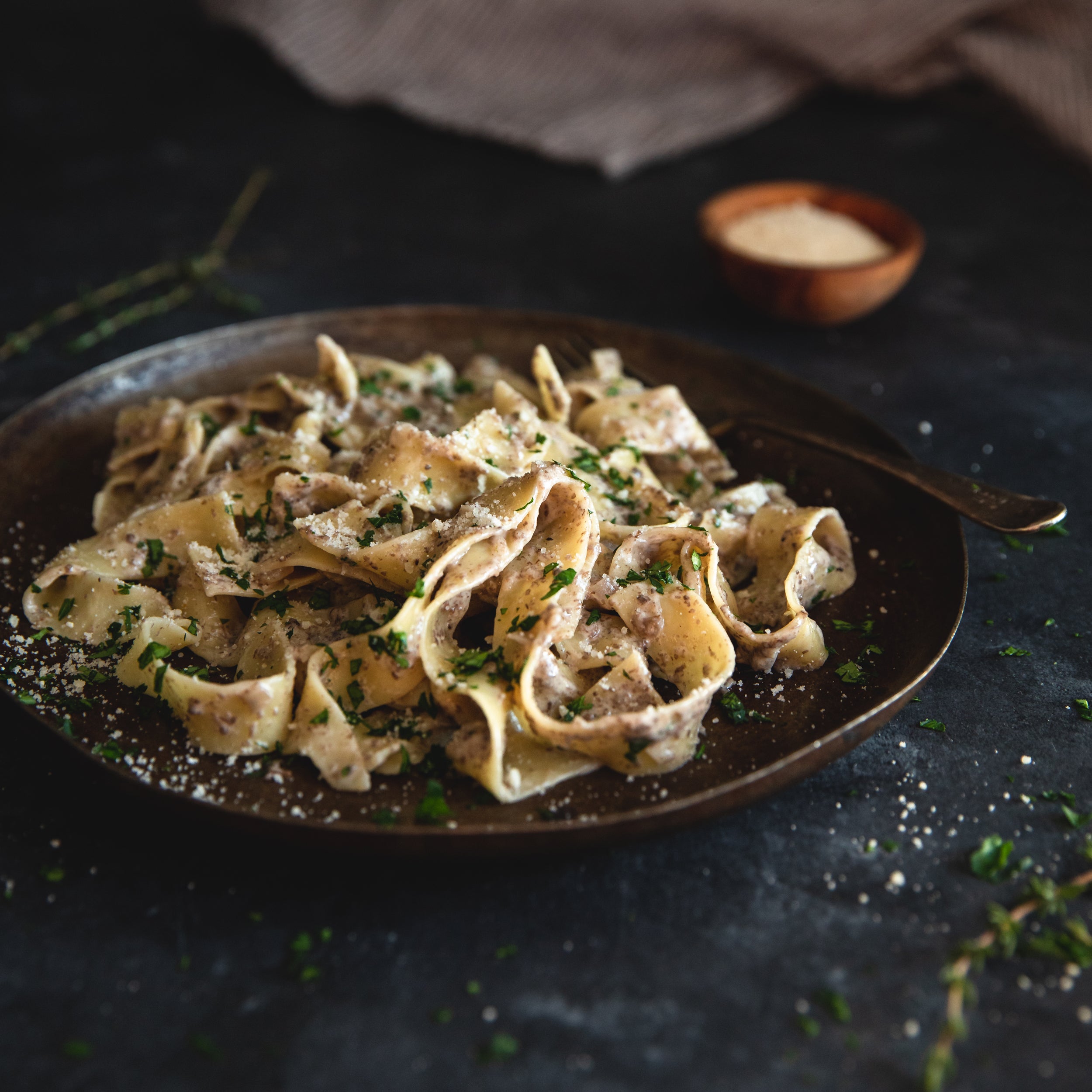 Creamy mushroom pappardelle served on a dark rustic plate with herbs and grated cheese