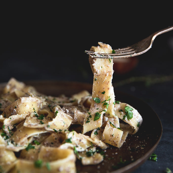 Fork lifting a twirl of creamy mushroom pappardelle garnished with parsley on a dark plate