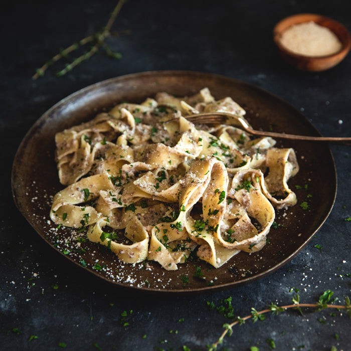 Overhead view of organic egg pappardelle in creamy mushroom sauce, garnished with parsley on a dark plate with a fork