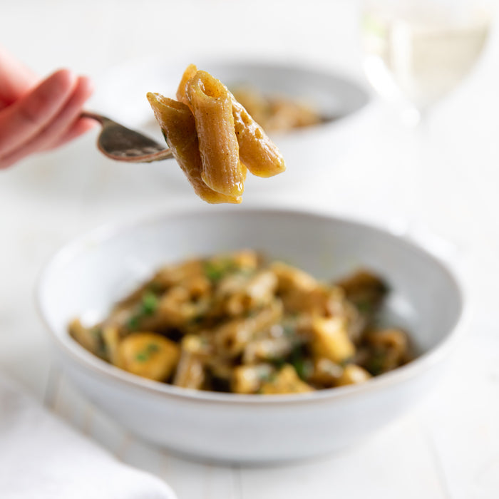 Fork lifting organic grain-free cassava penne over a bowl of sauced pasta on a white table