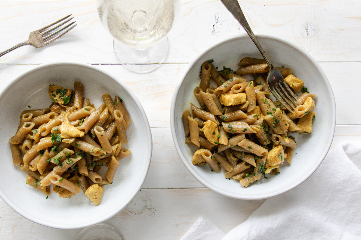 Coconut curry chicken tossed with grain-free cassava penne in white bowls on a light wooden table