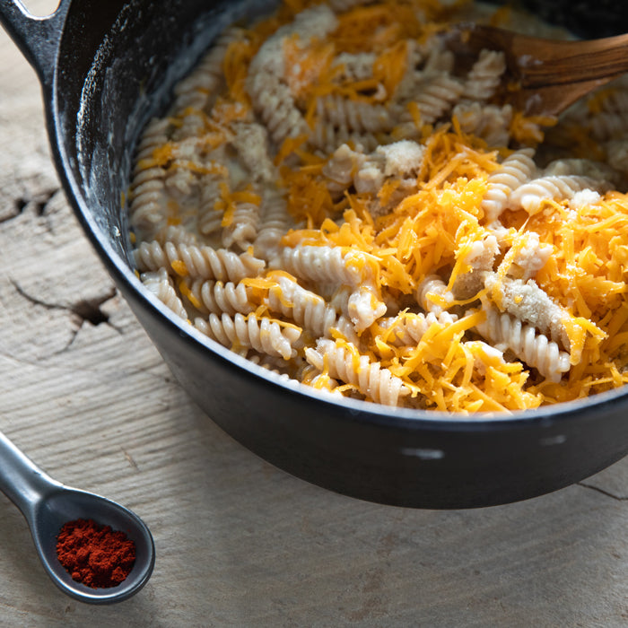 Fusilli one-pot mac and cheese in a black pot topped with shredded cheddar and breadcrumbs on a wooden board