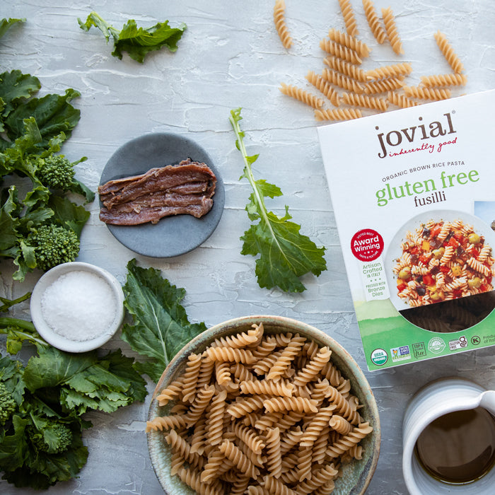 Top-down of organic gluten-free brown rice fusilli in a bowl with Jovial box, turnip greens, anchovies, salt, and olive oil