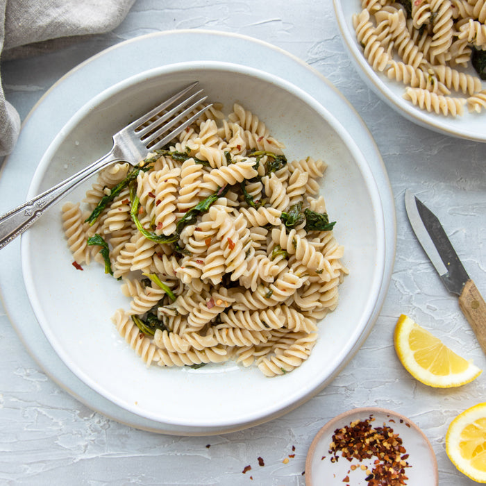Top-down view of gluten-free brown rice fusilli with spring greens, wilted greens and red pepper flakes on a white plate