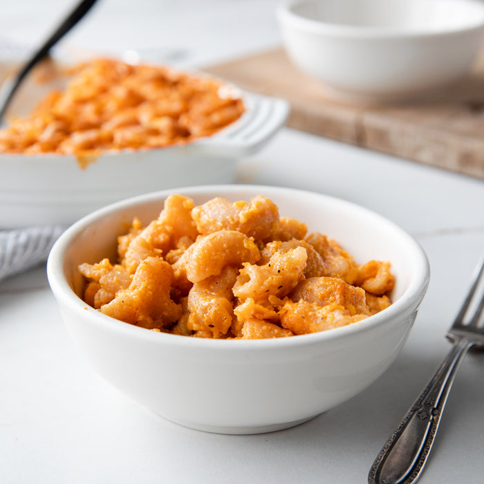 Front view of buffalo mac and cheese in a white bowl, creamy orange sauce coating shell pasta on a light countertop