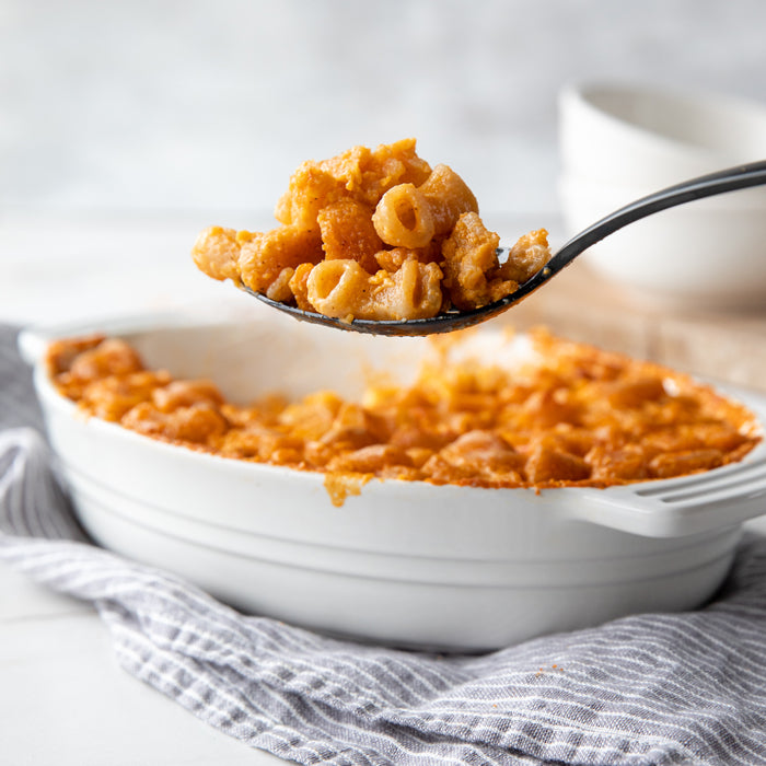 Spoonful of buffalo mac and cheese lifted from a baked white casserole dish on a gray striped cloth
