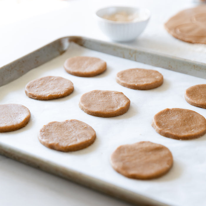 Unbaked einkorn digestive biscuit rounds arranged on a parchment-lined baking sheet ready to bake