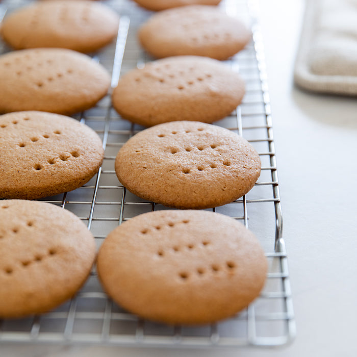Three-quarter view of Einkorn digestive biscuits on a cooling rack, golden-brown with fork-pricked tops