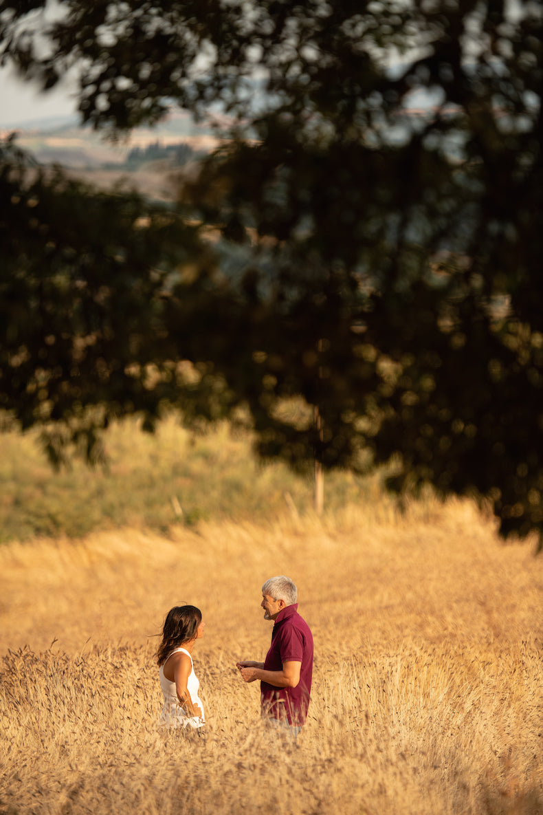 Two einkorn farmers talking in a golden einkorn wheat field under overhanging tree branches