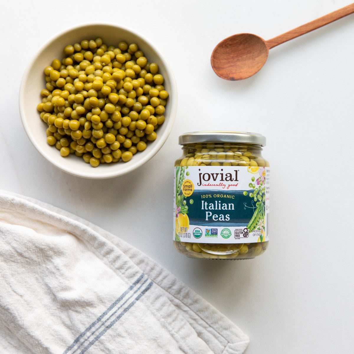 Top-down view of a Jovial jar of Italian organic peas showing the label beside a bowl of peas on a white surface
