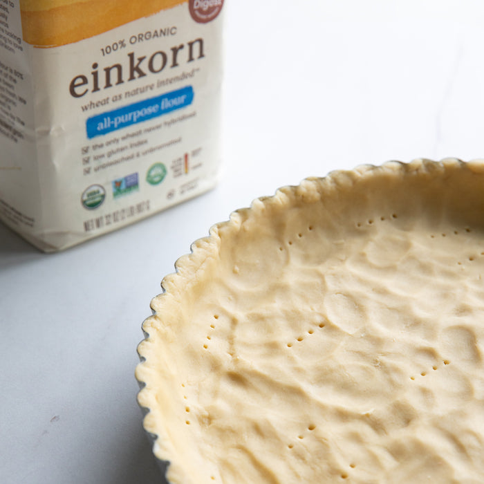 Unbaked tart crust pressed into a fluted 9-inch pan next to a bag of Jovial einkorn all-purpose flour on a light countertop
