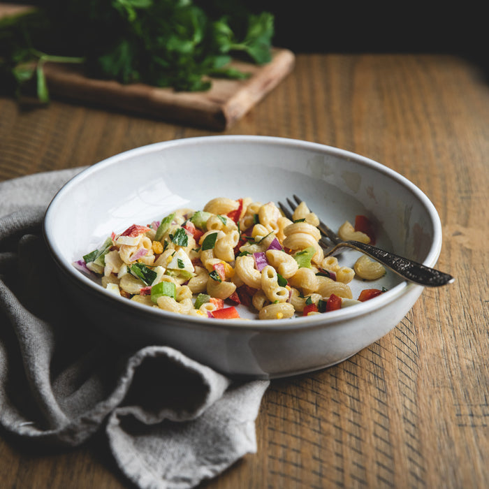 Prepared organic gluten-free rice and lentil elbow pasta salad with peppers and herbs in a white bowl on a wooden table
