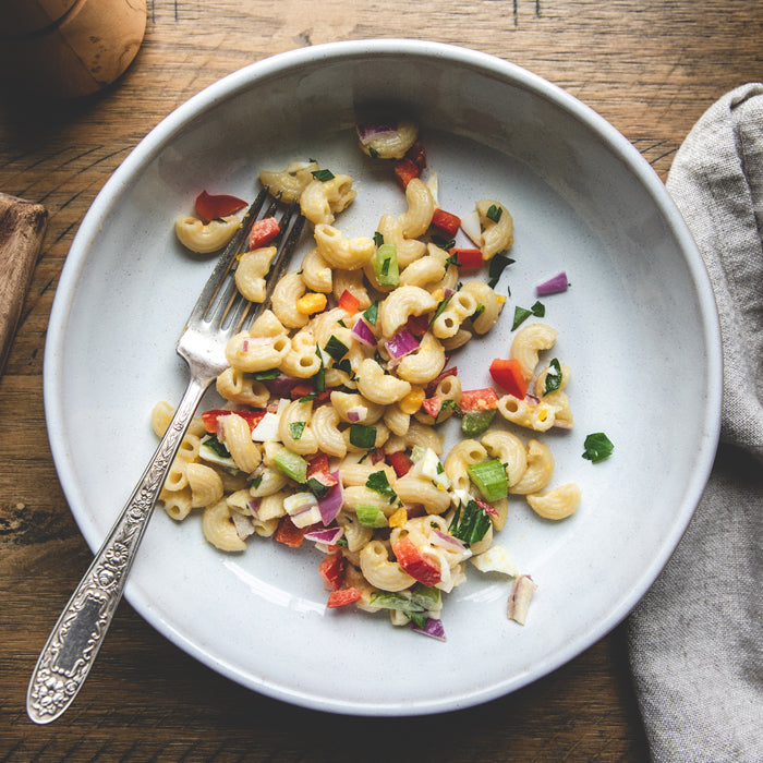 Bowl of cooked organic rice and lentil elbow pasta salad with herbs, vegetables, and a fork on a wooden table