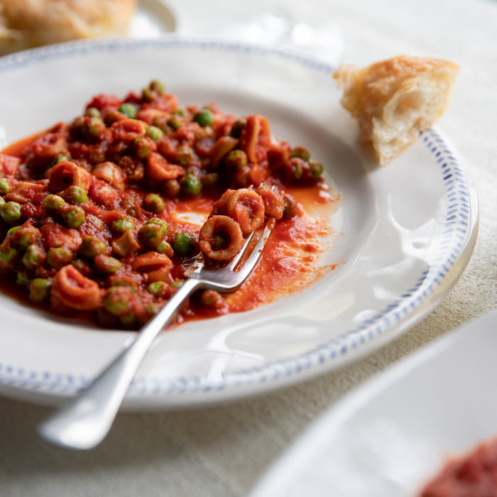 Calamari and peas in tomato sauce served on a white plate with a fork and torn bread beside it
