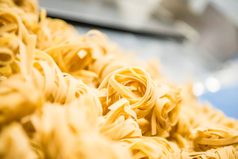 Close-up of artisan fresh tagliatelle pasta nests showing ribbon texture with blurred pasta-making equipment in background