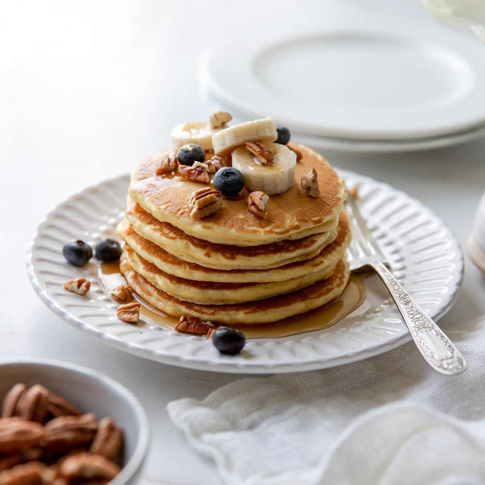Stack of golden organic einkorn pancakes topped with walnuts, blueberries, and maple syrup on a white plate