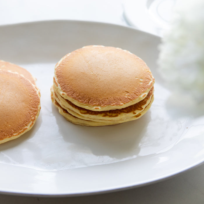 Top-down view of a small stack of golden einkorn pancakes showcasing fluffy edges on a white plate with a blurred white flower