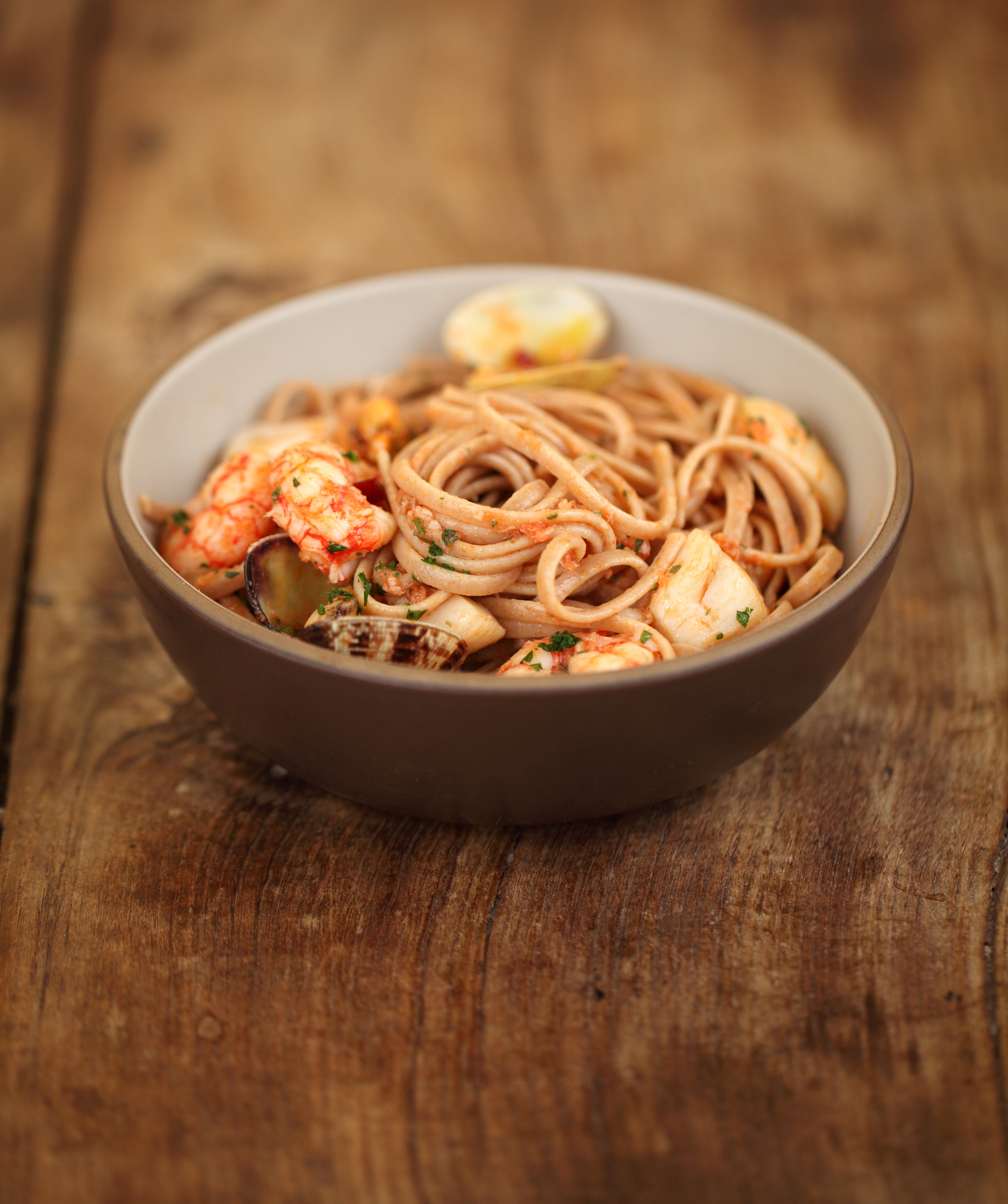 Bowl of einkorn linguine with seafood bouillabaisse served in a brown ceramic bowl on a wooden table