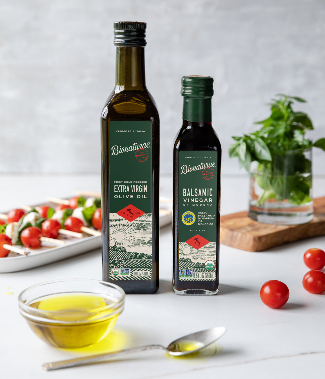 Bottles of olive oil and balsamic vinegar beside Caprese skewers of tomato, mozzarella, and basil on a kitchen counter
